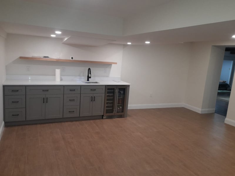 Small wet bar in open basement living space by Honorato Company in Boston